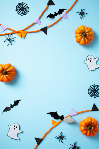 istock Halloween frame made of decorations, pumpkins, ghosts, bats, spiders, garland on light blue background. Flat lay, top view, vertical 2172312330