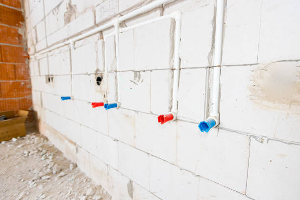 New unfinished plumbing installation exposed white PVC pipes mounted in the wall. Red and blue tubes are for hot and cold water.
