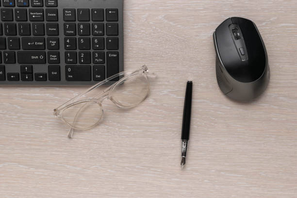 istock Office Desk with Keyboard, Glasses, Pen, and Mouse on Light Wood Surface 2172315154