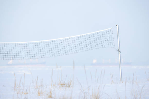 Net for beach volleyball is on empty sea coast covered with snow, winter sport background