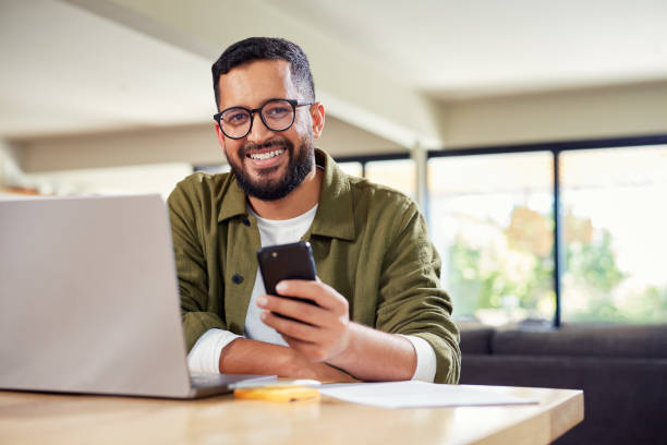 istock Smiling man using laptop and phone at home 2172317004