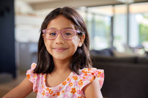 A young indian girl wearing glasses and a floral t-shirt while smiling at camera in a cozy home. Close up of happy middle eastern girl with eyeglasses looking at camera. Portrait of a cheerful little middle eastern child with long hair and glasses, smiling warmly with copy space.