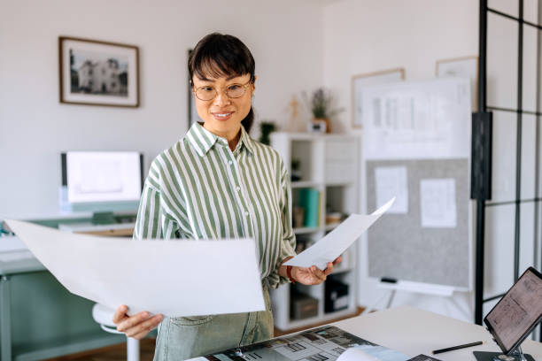 istock Beautiful female architect analysing blueprints at her home office 2172317357