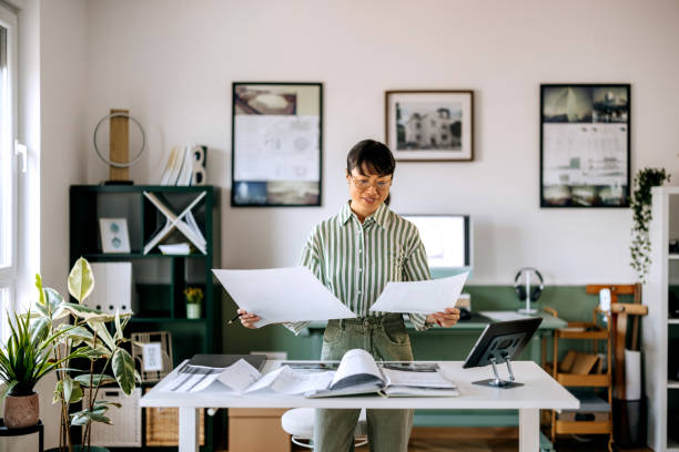 istock Beautiful female architect analysing blueprints at her home office 2172318215