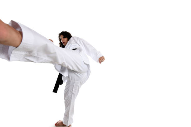 Fifteen year old male teenage karate black belt doing a side back fist, studio shot against a black background