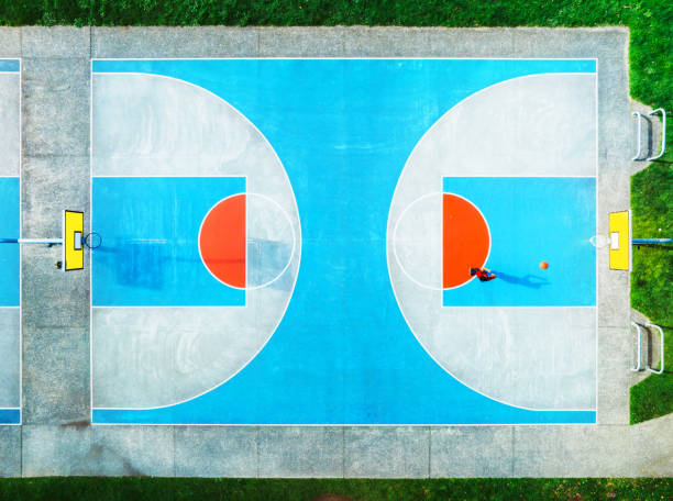 Overhead view of a boy playing basketball in blue basketball court with distinct marking pattern.