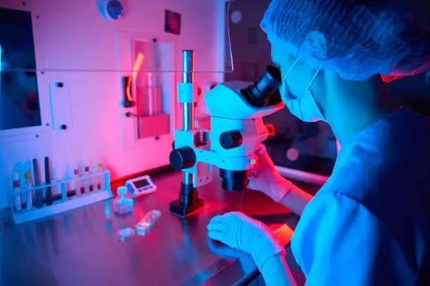 Photo of Embryologist analyzing samples under a microscope with colored lights
