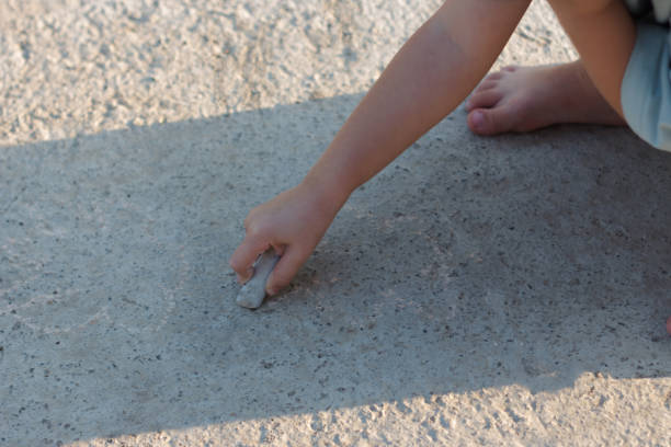 A child draws on the asphalt with crayons in summer
