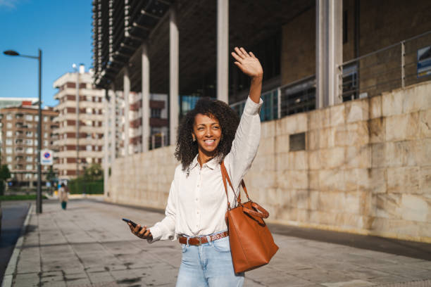 istock Female executive waving and using a cellphone as she walks along a city sidewalk 2172342785