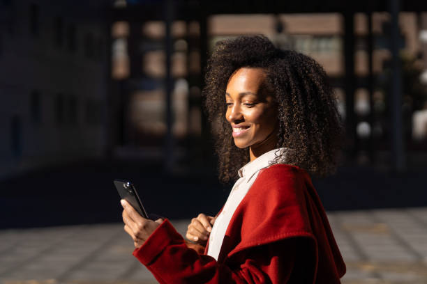 istock Young working woman happily using her smartphone outside in the sunshine 2172342925