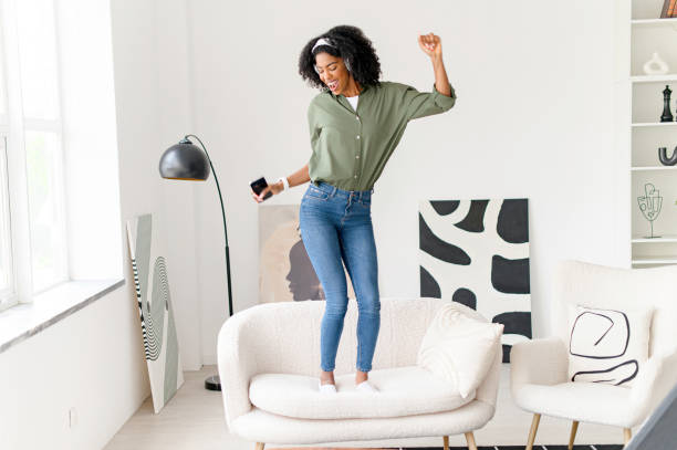 istock In a dynamic pose, the woman dances on a couch with her smartphone in hand 2172345145