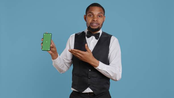 istock Hotel worker bellhop points at phone with isolated mockup display 2172345154
