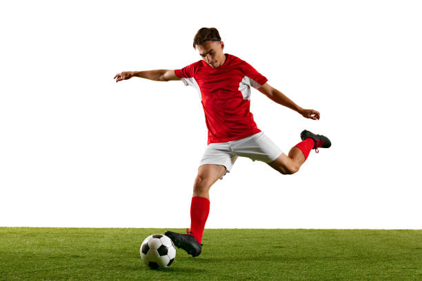 istock Young athletic man, football player, in red-white uniform, practicing powerful kick on green field against white studio background. 2172355190