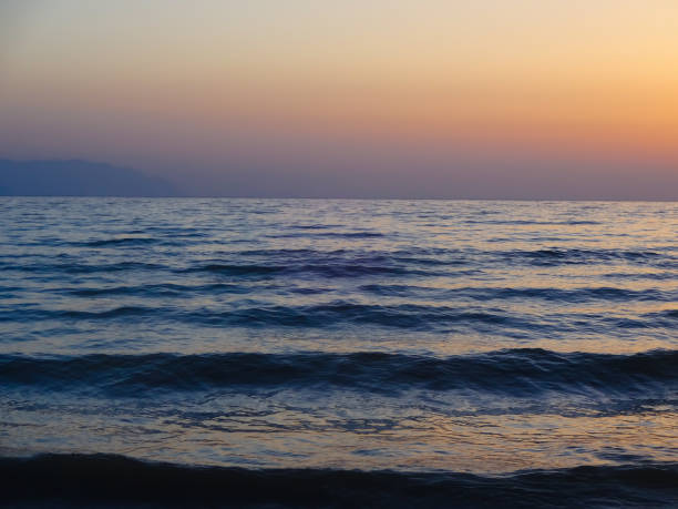 The sun sets on the horizon over a calm sea with gentle waves. Ideal for content about seaside relaxation and tourism.