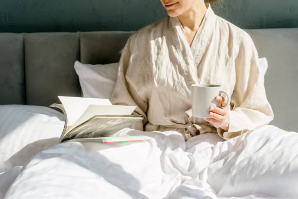 Woman sitting on bed holding coffee cup, reading book