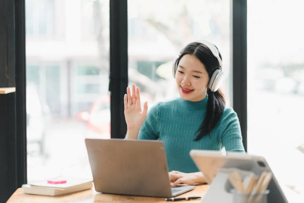 istock Engaged woman with headphones waving while using laptop in cafe 2172364024