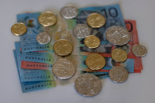 Australian dollar bills and coins Australian dollar coins over a stack of Australian dollar bills, seen at an angle over an off white table top. Photo with shallow depth of field. australian 5 cents stock pictures, royalty-free photos & images