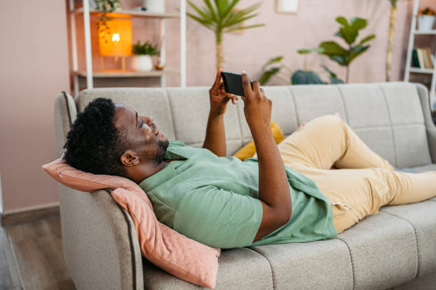 istock Young Man Playing Video Games On The Phone While Lying On The Sofa At Home 2172367412