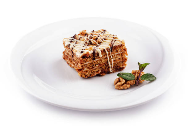 Slice of layered cake with nuts and chocolate sauce is presented on a white plate, ready to be enjoyed