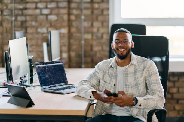 African American entrepreneur takes a break in a modern office, using a smartphone to browse social media, capturing a moment of digital connectivity and relaxation amidst his business endeavors.