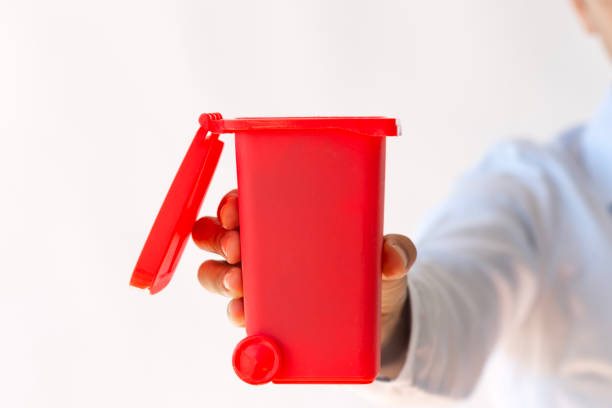 Woman in front of a garabe truck throwing a waste bag in a bin and gesturing thumbs up isolated on white background