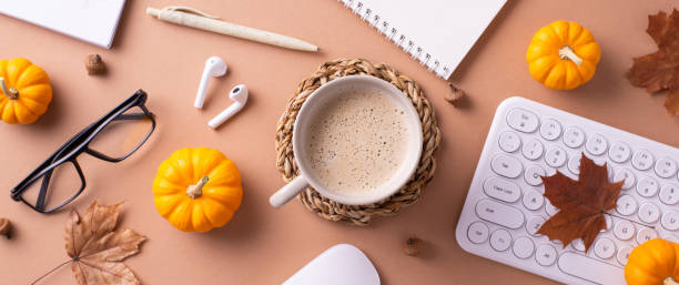 A cozy autumn-themed workspace featuring a coffee cup, mini pumpkins, and office supplies creating a warm atmosphere
