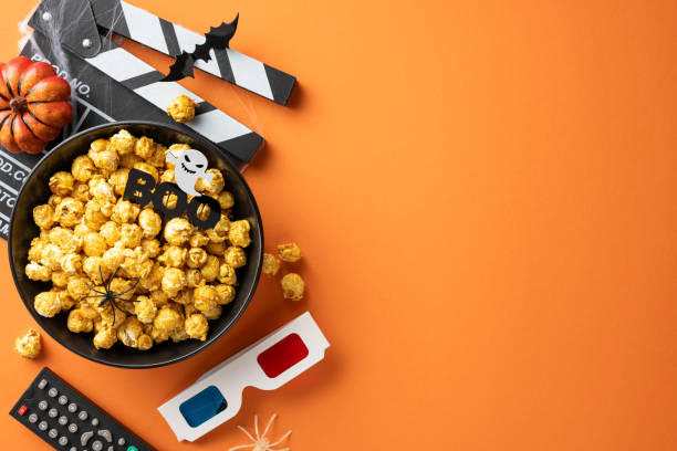 istock Halloween-themed setup with popcorn, movie clapperboard, pumpkin, and spooky decorations on an orange background 2172401488