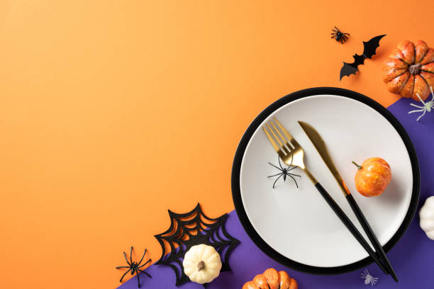 istock Halloween table setting with white plate, pumpkins, bats, and spider decorations on an orange background 2172401529