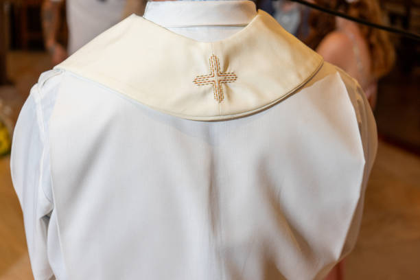 A priest, viewed from behind, wears a flowing white chasuble adorned with delicate gold embroidery, standing in a sacred space, symbolizing devotion and solemnity in religious ceremony.
