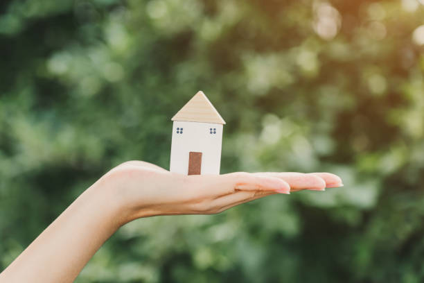 istock A woman's hand is holding a small wooden house. 2172422082