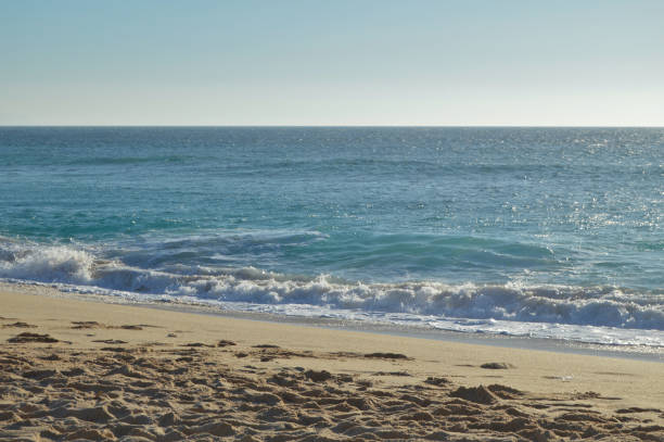 Calm ocean scene with gentle waves washing ashore on a sandy beach under a clear sky. Evokes peace, summer, and a sense of escape. Ideal for travel, relaxation, or nature themes.