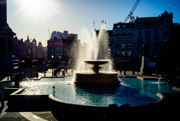 One of the famous fountains in Trafalgar Square, City of Westminster, London, silhouetted against bright sunlight.
