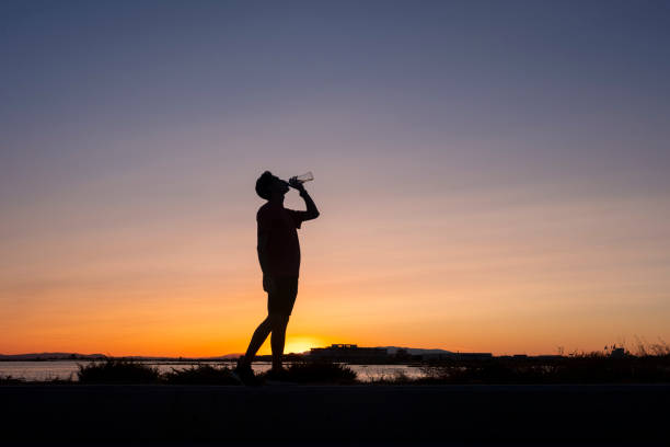 Athlete drinking water while exercising on the seashore at sunset.