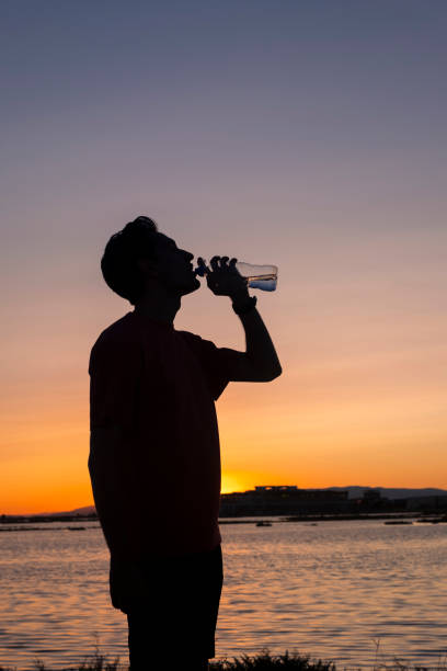 istock Athlete drinking water while exercising on the seashore at sunset. 2172435738
