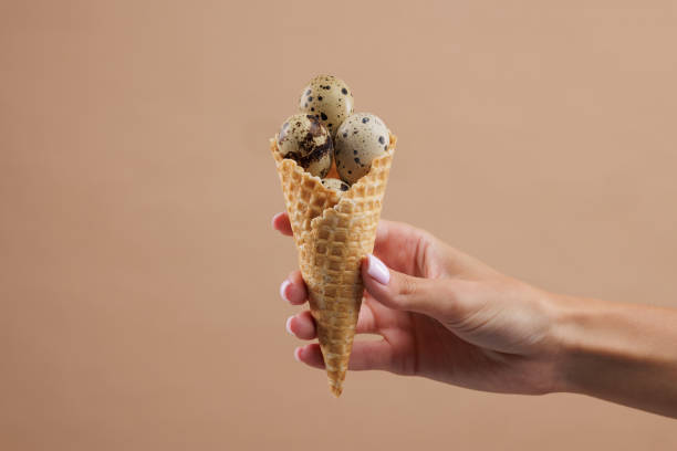 istock Hand holding a waffle cone filled with quail eggs on a beige background. 2172440865
