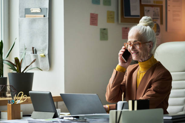 istock Elderly Woman Smiling While Talking on Phone in Office Setting 2172448417