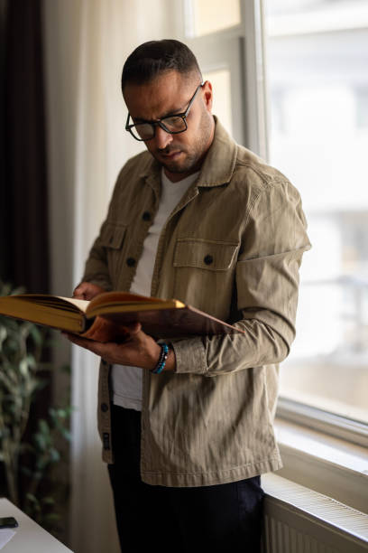 istock Young man reading book in the library 2172451748