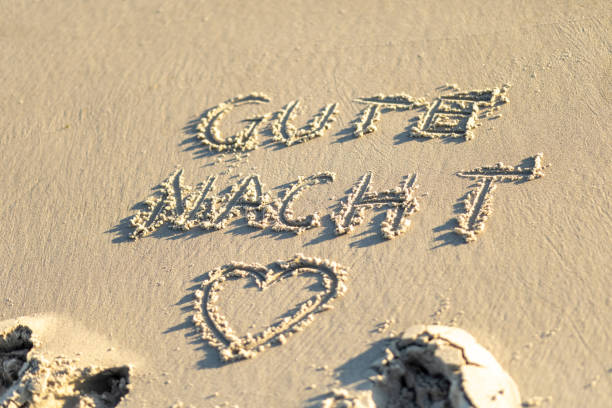 A beautiful sandy beach features a heartfelt Gute Nacht written in the sand, complemented by a heart symbol and the soft sound of waves in the background.