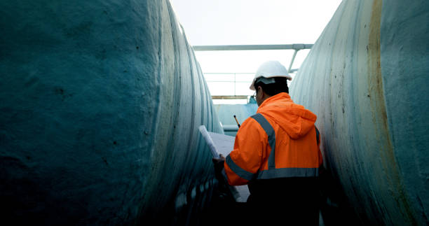 istock Mechanical Engineer wearing orange safety jacket and white hardhat with laptop  and blueprint working on horizontal water tanks at construction site 2172471105