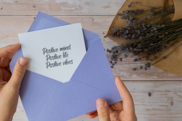 istock Female hands taking paper card note with text POSITIVE MIND LIFE VIBES from violet envelope. Lavender flower. Top view, flat lay. Concept of mental spiritual health self care wellbeing 2172476125