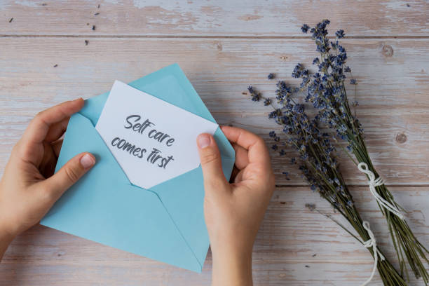 istock Female hands taking paper card note with text SELF CARE COMES FIRST from blue envelope. Lavender flower. Top view, flat lay. Concept of mental spiritual health self care wellbeing 2172476316
