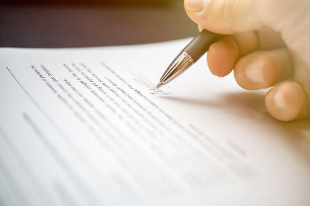 A focused hand writes a signature on official documents, illustrating the concept of legal agreements, personal commitment, and professionalism in business environments.