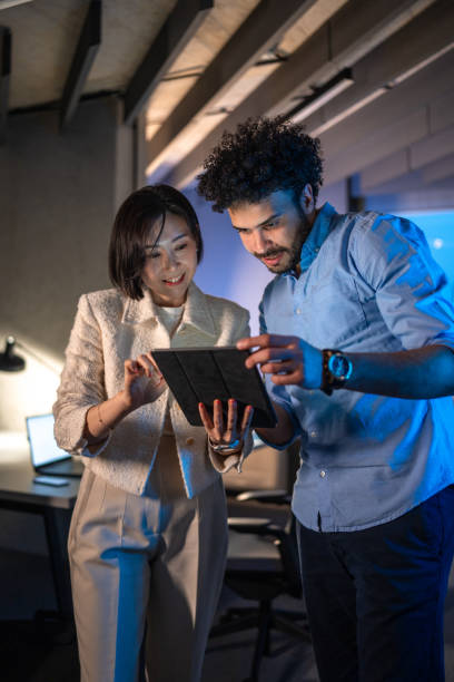 Diverse Executives Reviewing Data on Tablet in Office at Night