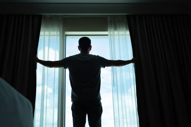 istock Young man opening his window curtains letting in the light. 2172484483