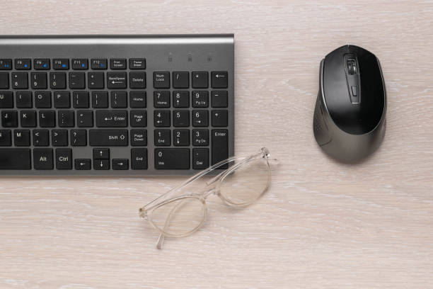 Modern Office Workspace with Wireless Keyboard, Mouse, and Glasses on Wooden Desk