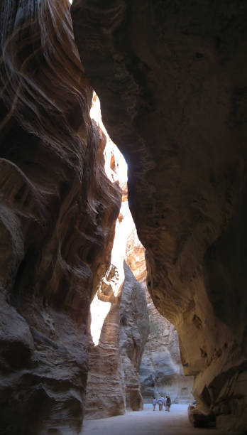 Group of distant people Walking in famous Petra Siq Canyon with narrow stone walls and aqueduct