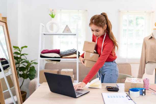 istock A young woman is holding several boxes while preparing orders for her online clothing business. She is smiling and working in a bright, organized workspace. 2172516688
