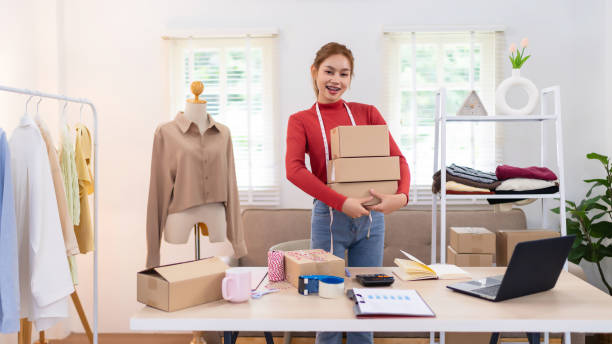 istock A young woman is holding several boxes while preparing orders for her online clothing business. She is smiling and working in a bright, organized workspace. 2172516689