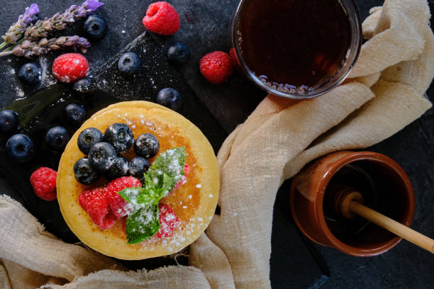 pancakes with berries and honey on dark background top view