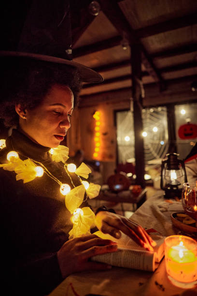 istock Black woman dressed as a witch reading a book on Halloween. 2172531394